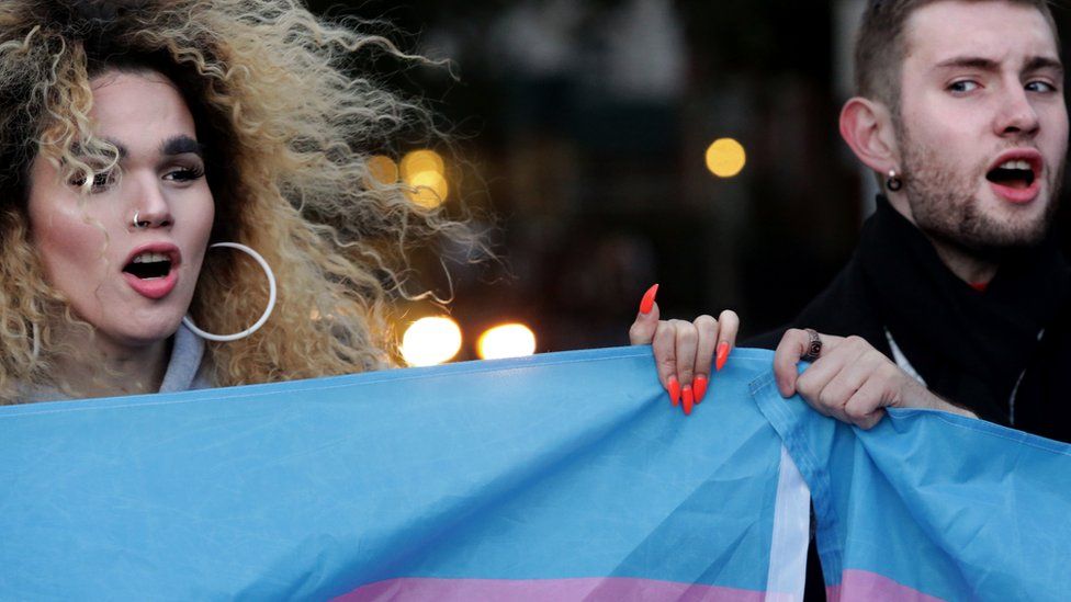 Two protestors hold up a flag for Transgender and Gender Non-comforming people