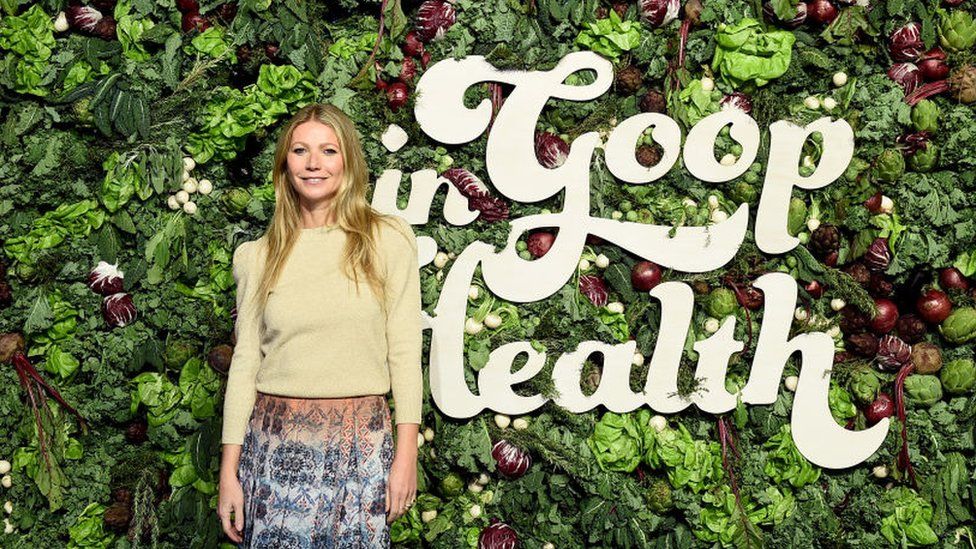 Gwyneth Paltrow stands in front of a wall of vegetables