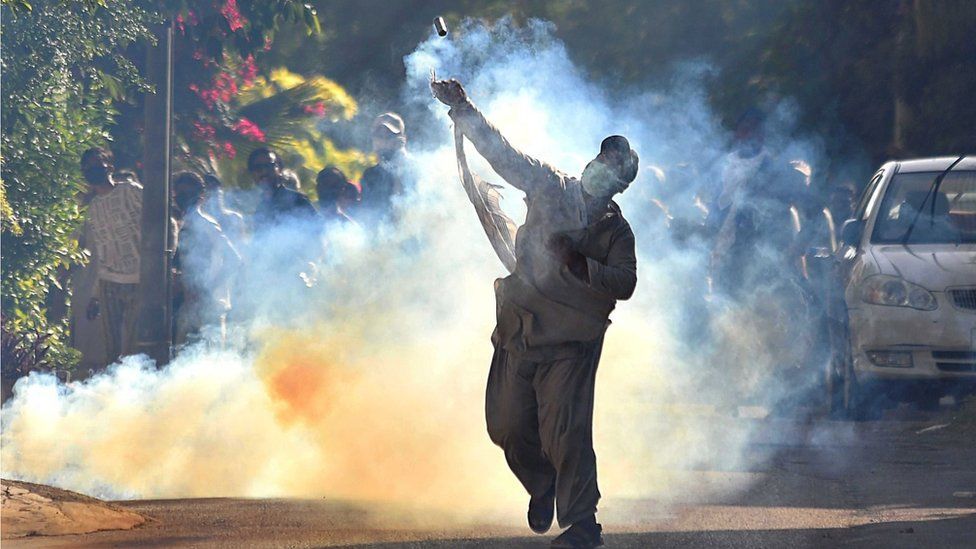 A supporter of former Prime Minister and head of opposition party Pakistan Tehrik-e-Insaf, Imran Khan, throws a tear gas cannister back during clashes with security forces after violent protests broke out across the country following Khan's arrest, in Karachi,