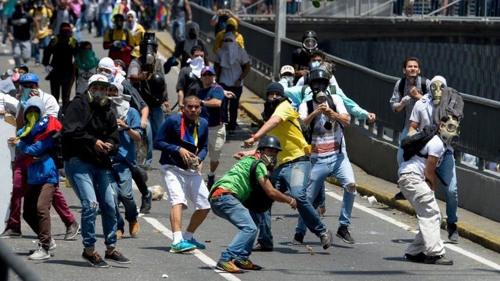 Demonstrators protesting against President Nicolas Maduro's government, some of them wearing gas masks, throw stones at riot police in Caracas on April 8, 2017.