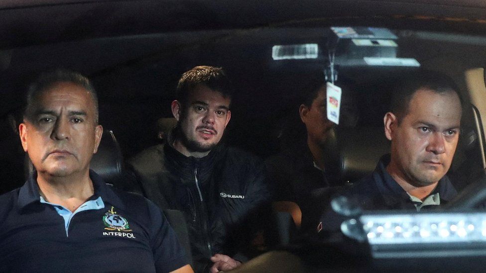 Police officer driving and in passenger seat, van der Sloot in backseat.