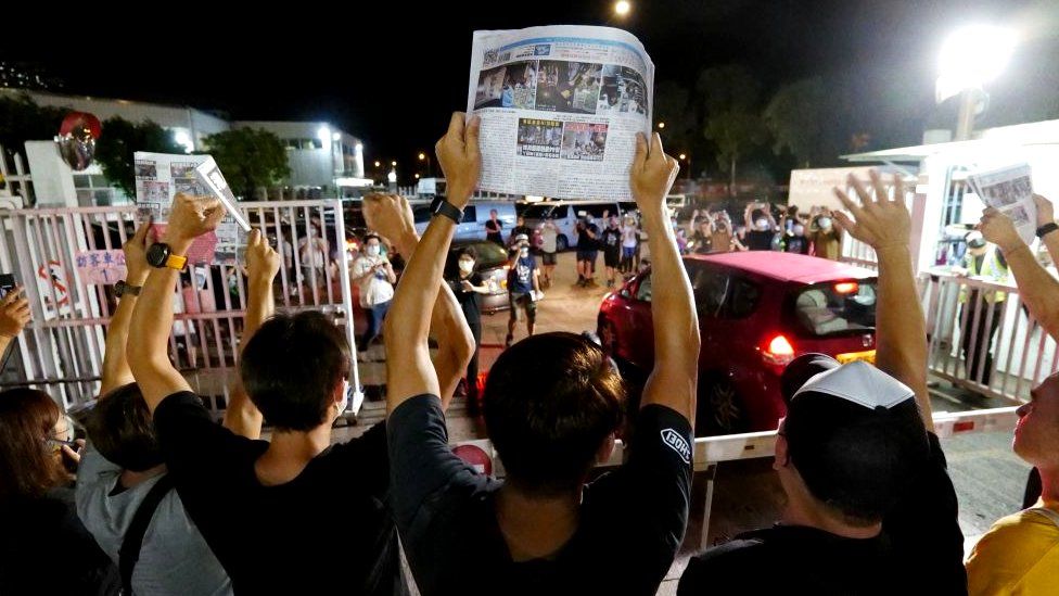Apple Daily journalists hold freshly-printed copies of the newspaper's last edition while acknowledging supporters gathered outside their office in Hong Kong