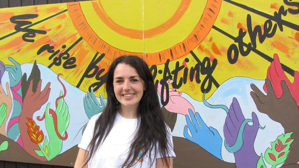 Lara Deffense coordinates Refugee Week UK and was at the unveiling of the mural pictured standing in front of the mural