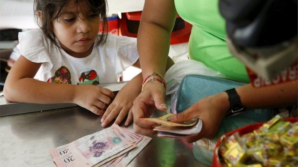 A girl looks at Venezuelan bolivar notes while her mother counts them to pay the cashier at a supermarket checkout line in Caracas on 20 October, 2015.