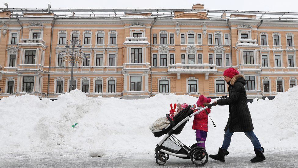 A woman pushes a pram past piles of snow in Moscow