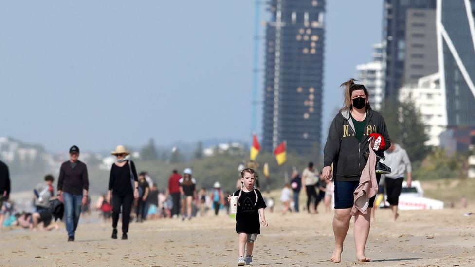 People wearing masks walk along the beach at Surfers Paradise