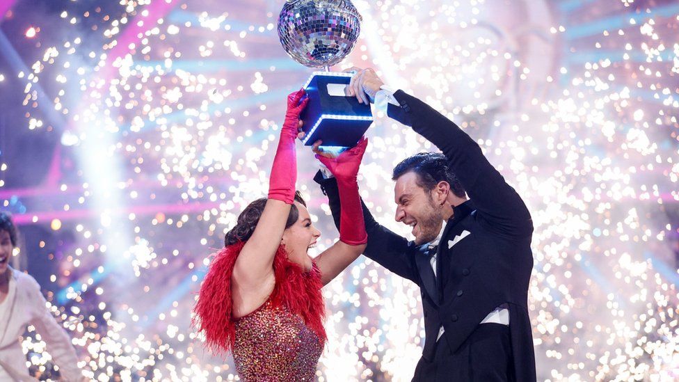 Strictly Come Dancing 2023 Ellie Leach and Vito Coppola holding the Glitterball trophy above their heads with fireworks visible behind them