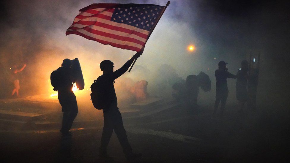 A protester waves an American flag while walking through tear gas fired by federal officers during a protest in front of the Mark O Hatfield US Courthouse in Portland, Oregon, 21 July 2020