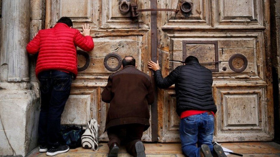 Men kneel and pray in front of the church's doors in Jerusalem's Old City