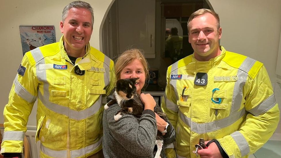 two firefighters and a woman holding a cat