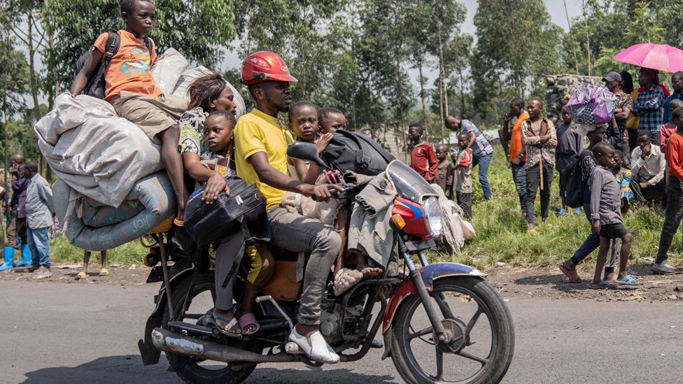 A family flees fighting on the back of a motorbike