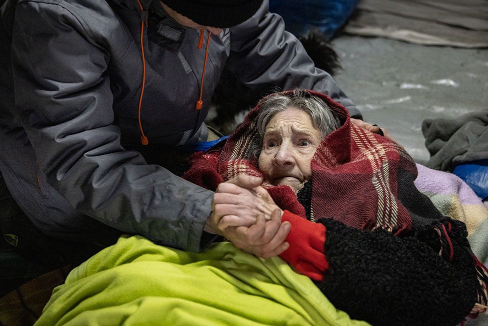 An elderly woman is helped to cross an improvised path along a destroyed bridge to flee the city of Irpin, Ukraine, on 8 March 2022
