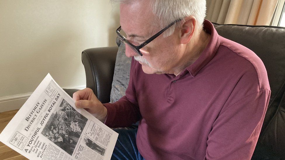 Colin Spence reading an old newspaper article of the time the Queen came to his former home in Bletchley