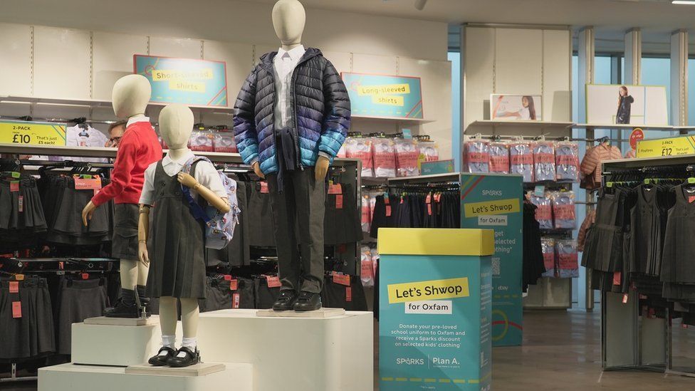 A school uniform department in a shop, with mannequins in the clothing and a box to drop used uniform in to.