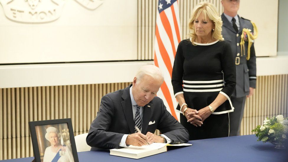 President Joe Biden seen signing a book of condolences to the Queen as First Lady Jill Biden stands behind him