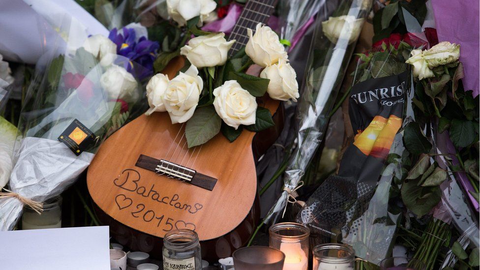A guitar with white roses lies in front of the music venue Bataclan in Paris