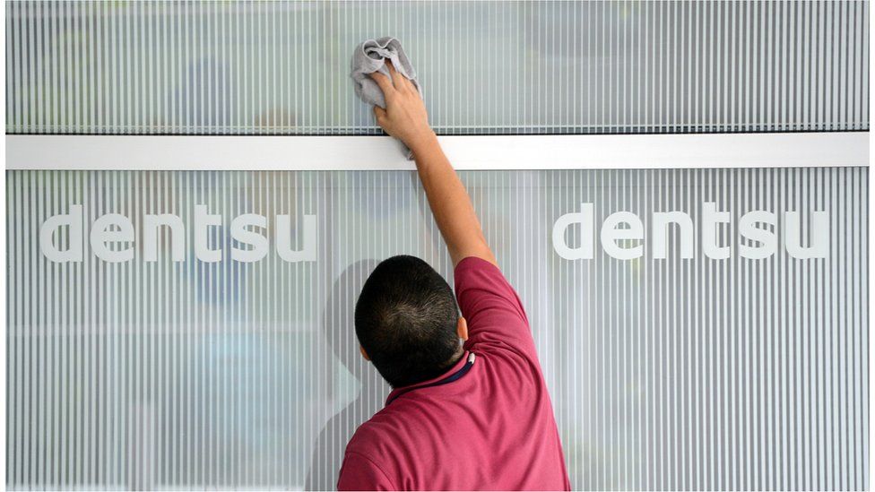 A man cleans a logo on a wall for Japan's Dentsu advertising agency