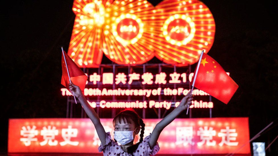 Девушка в маске размахивает национальным флагом во время столетия основания выставки фонарей КПК в Expo Garden 25 июня 2021 года в Ухане, провинция Хубэй. Китай.