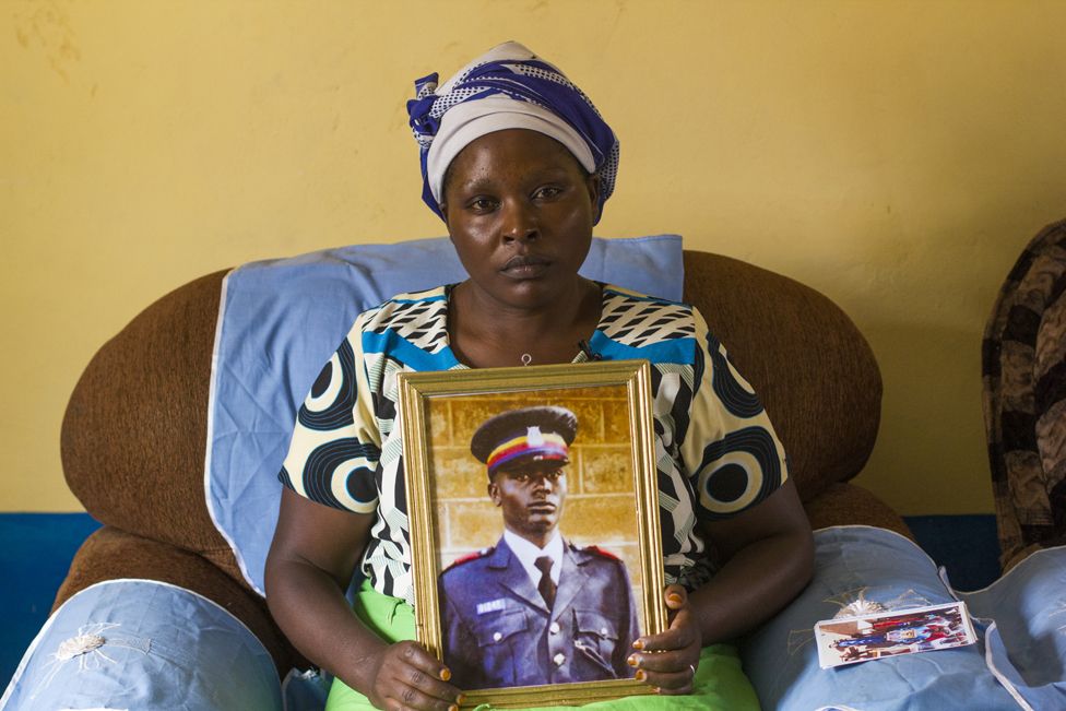 Ирен Ндуку Касёки держит портрет своего покойного мужа Джеффри Касёки, полицейского, который погиб, пытаясь спасти песок своего сообщества