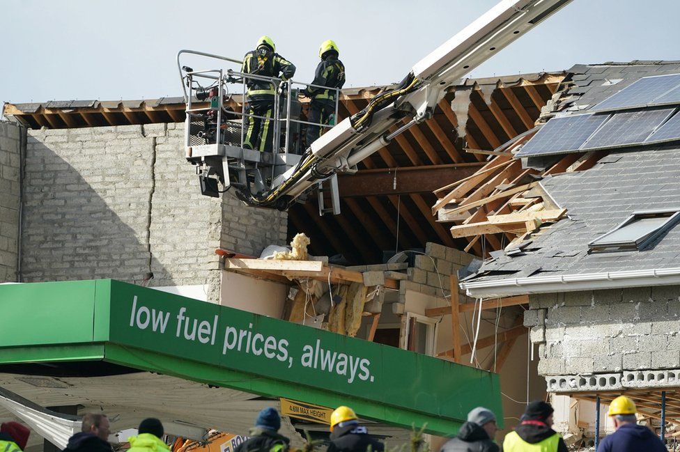 Firefighters on a mechanical platform assess the damage caused to the service station and a nearby apartment block