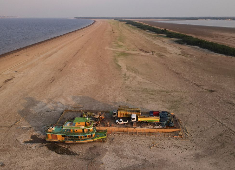 A barge carrying three trucks, 2,000 empty cooking gas cylinders and a backhoe, stranded on a sand bank of a diminished Rio Negro river