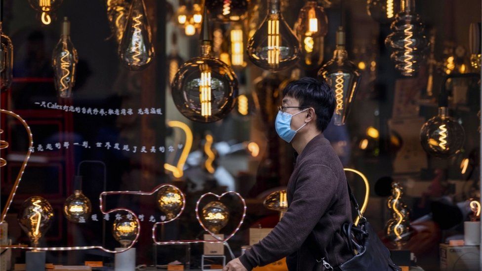 A man wearing a mask for protection walks in front a shop window selling bulbs and lighting in Shanghai, China