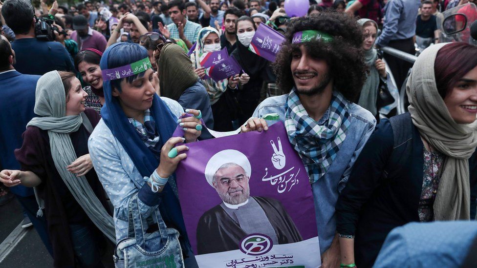 Supporters of newly re-elected Iranian President Hassan Rouhani hold a placard bearing a portrait of him as they take to the streets to celebrate his victory in downtown Tehran