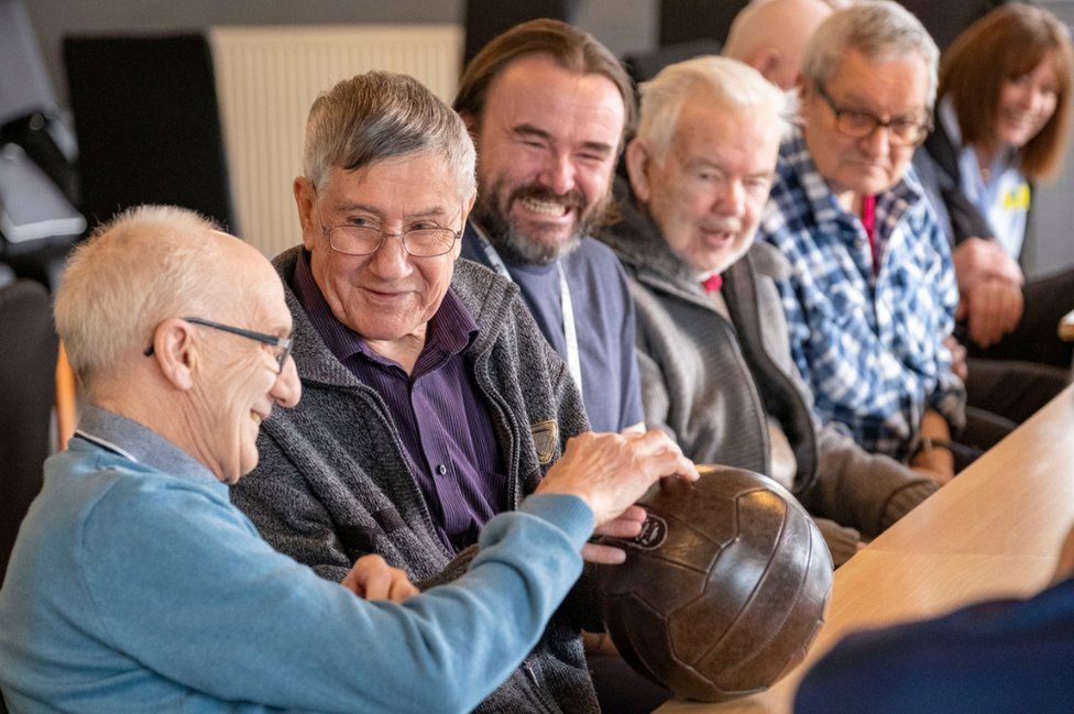 An elderly man smiles as he picks up an old football as part of a Sporting Memories session