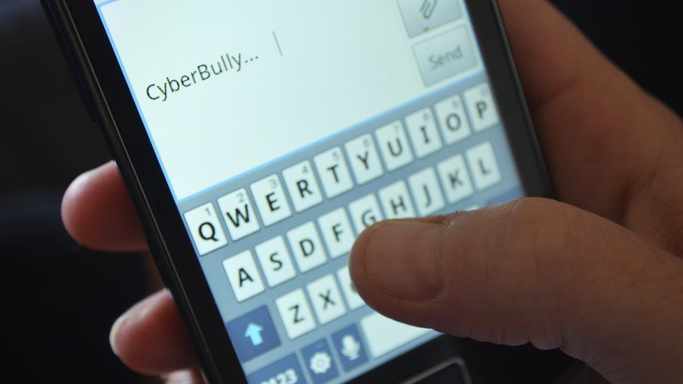 Hand typing on a phone saying cyberbullying