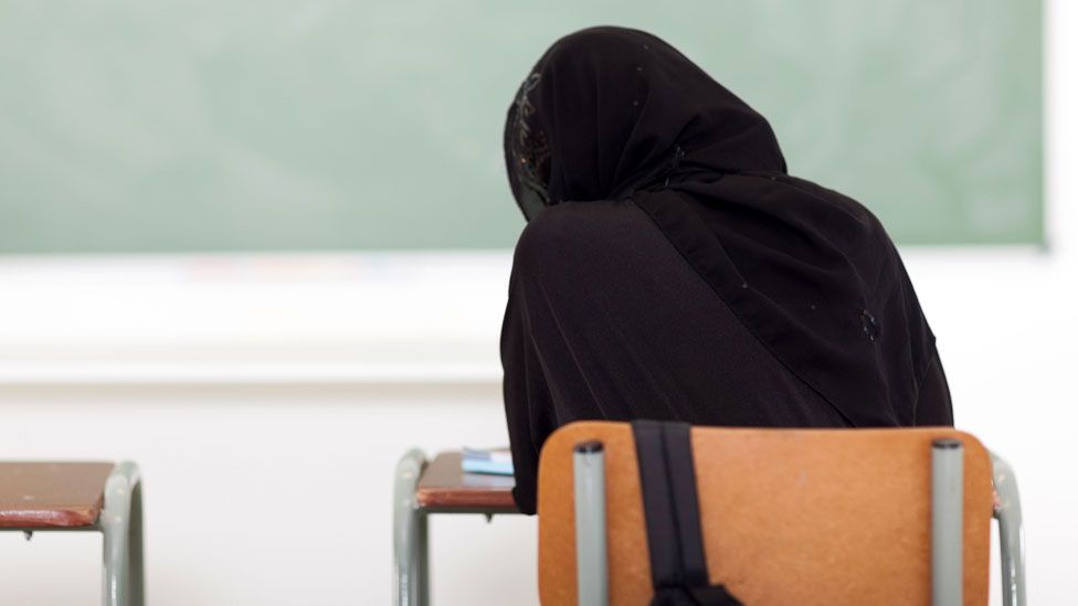 Women wearing a black hijab sits in front of a chalkboard