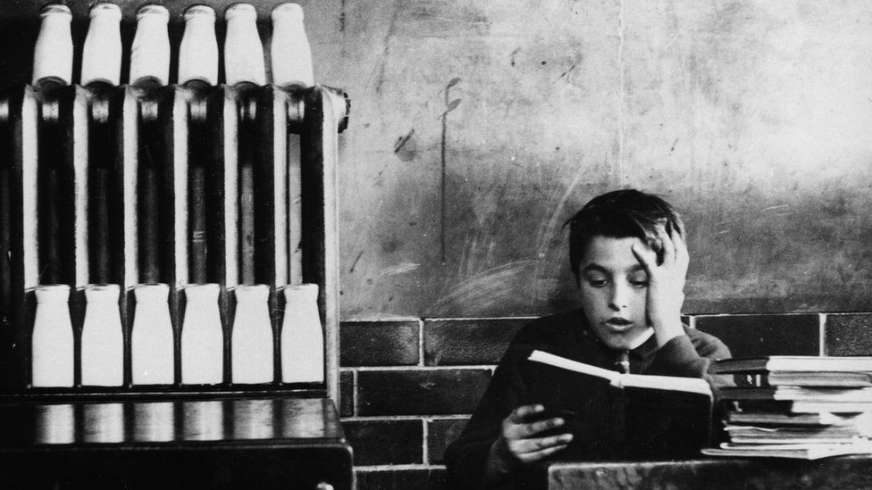 A schoolboy reads at his desk while a radiator takes the chill off the pupils' daily milk ration at an Ogmore Vale school, Glamorgan, in mid-winter, 1937