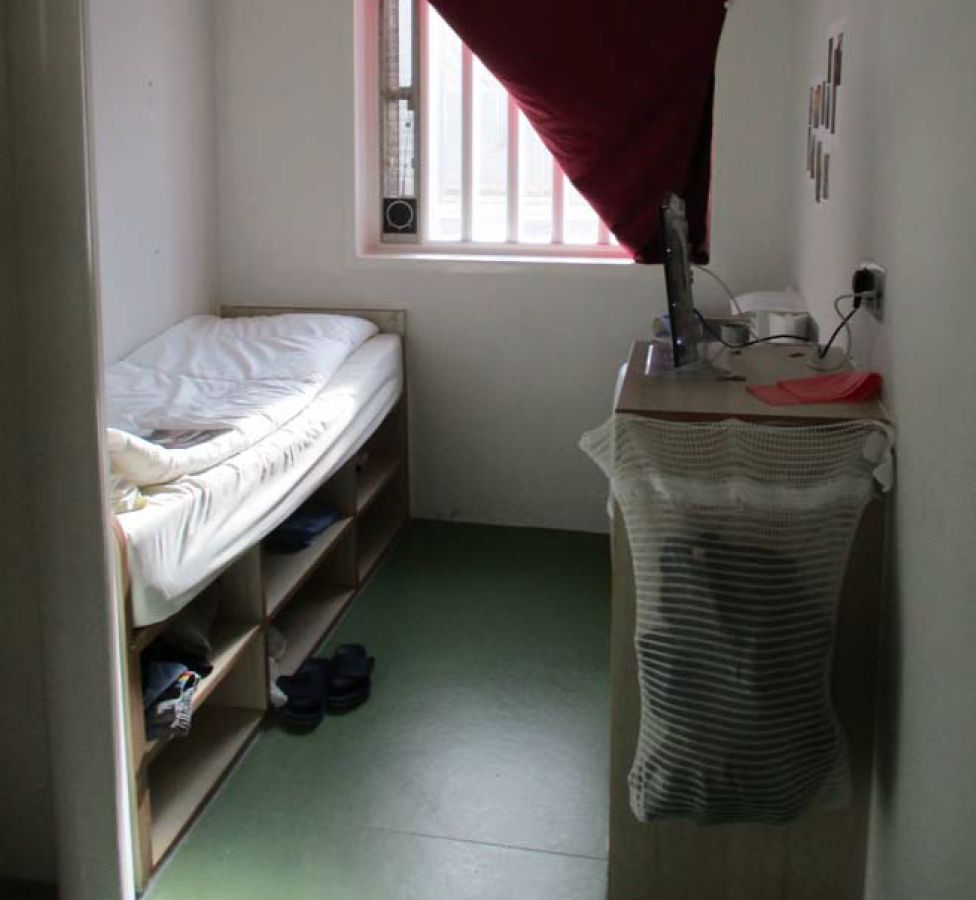 A prison cell with a single bed and bars on the windows