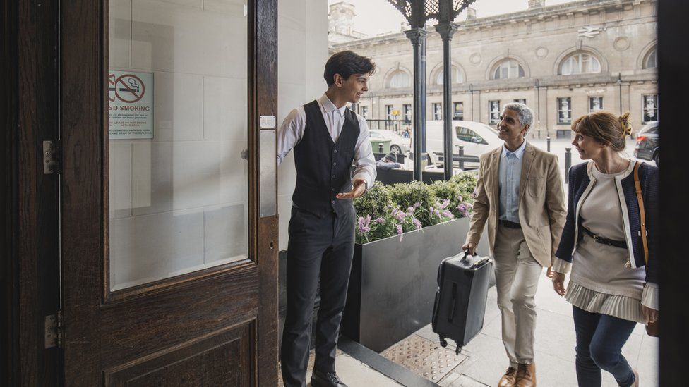 A young hotel doorman welcomes guests to a hotel