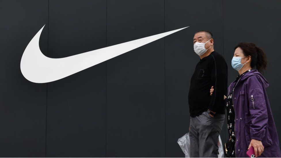 Two people walk in front of the Nike logo of the Nike flagship store at Wangfujing Pedestrian Street in Beijing, China.