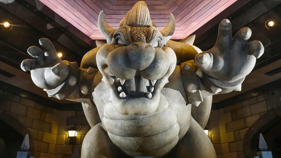 A statue of Bowser is seen with arms raised in a scaring pose in the Nintendo theme park