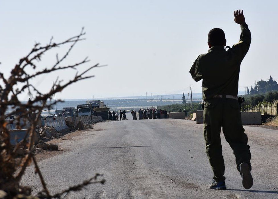 A fighter from the Kurdish People's Protection Units (YPG) gestures at displaced Syrians walking towards a Kurdish controlled checkpoint between the rebel-held town of Azaz in northern Syria and the city of Afrin, along Syria's northern border with Turkey, as they attempt to cross in June 2017