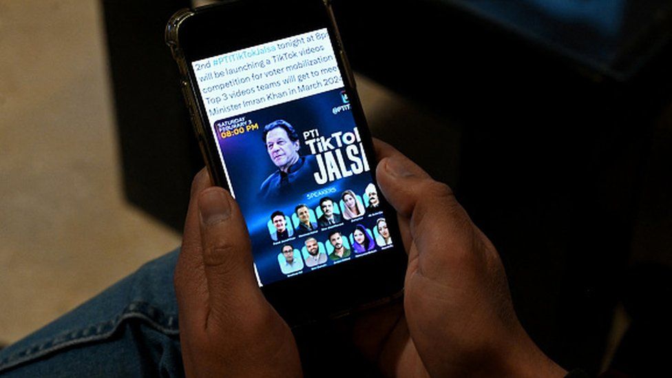 Pakistan's former prime minister Imran Khan's supporter listens to a virtual election campaign on a phone