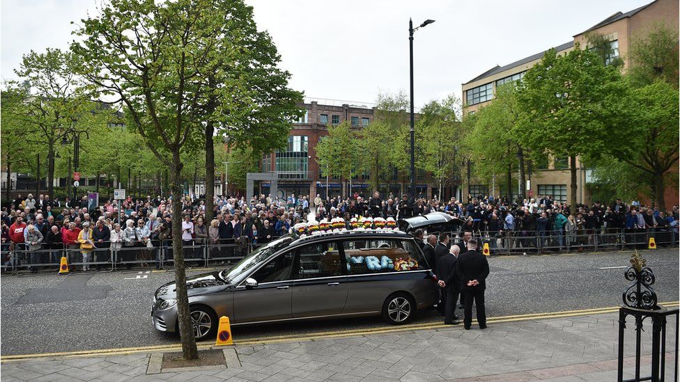 The funeral hearse arrives outside St. Anne's Cathedral in front of crowds of mourners.