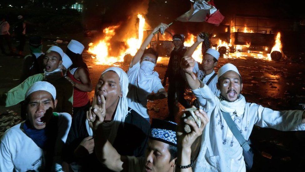 Muslim protesters chant slogans near burning police trucks during a clash with the police outside the presidential palace in Jakarta, Indonesia, Friday, Nov. 4, 2016.