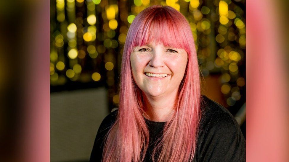 Sybil Bell, who has pink hair,smiling with lights in the background