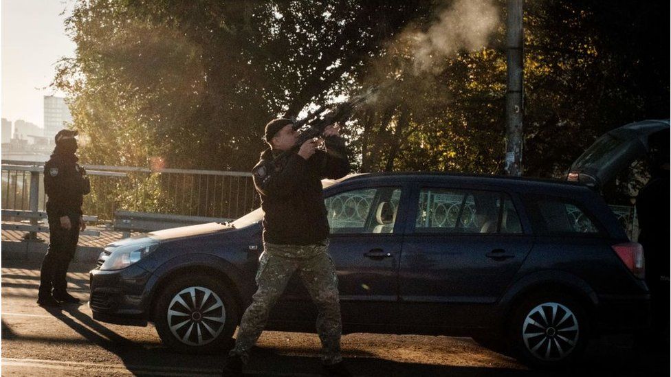 An officer fires at a flying drone stood in front of car.