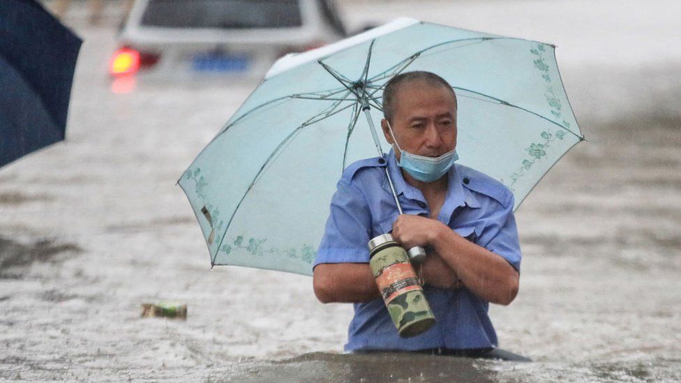 This photo taken on July 20, 2021 shows a man wading through flood waters