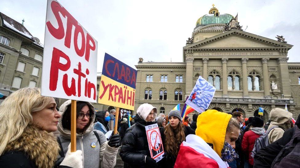 Women hold placards in front of the Swiss House of Parliament during a national demonstration against the war in Ukraine that gathered around 10,000 participants in Swiss capital Bern