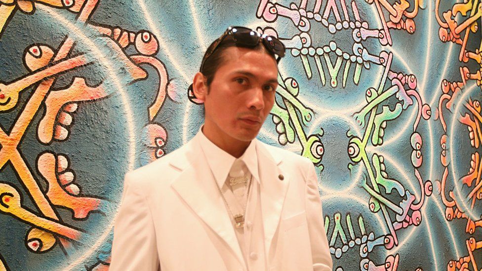 Ozzie Juarez stands in front of artwork at Beyond the Streets exhibition