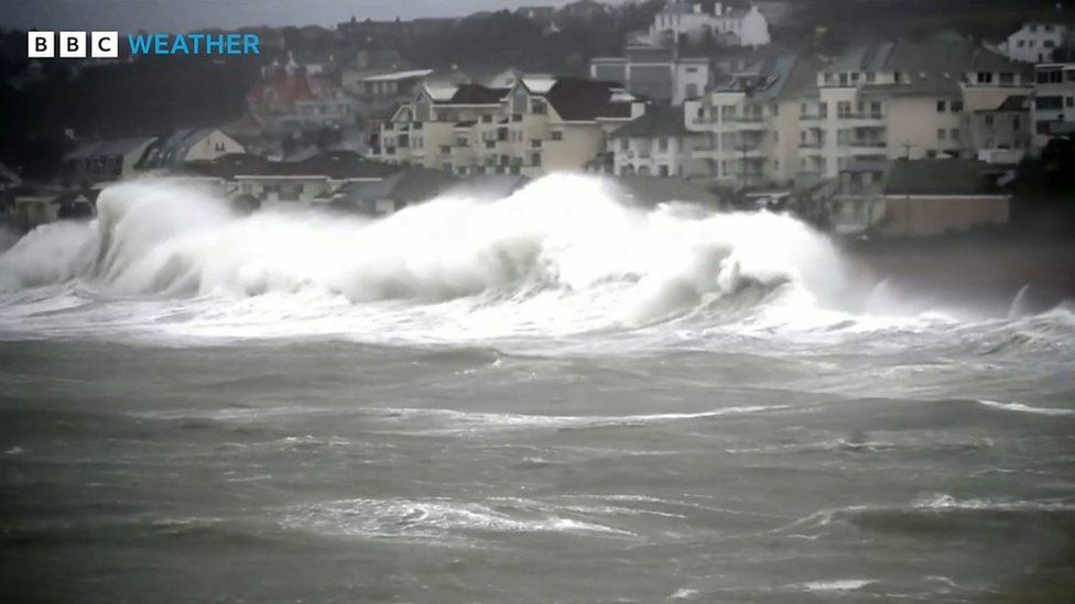 Massive waves crash up against the shore line with houses behind