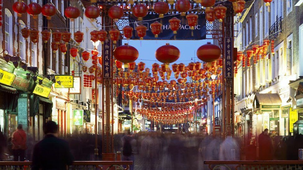 A time-lapse image showing blurry crowds moving underneath lanterns in Chinatown in central London