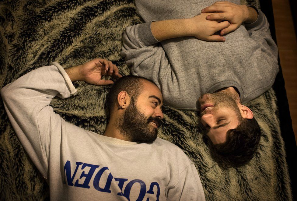 Elias lies on a bed with his boyfriend Marwan