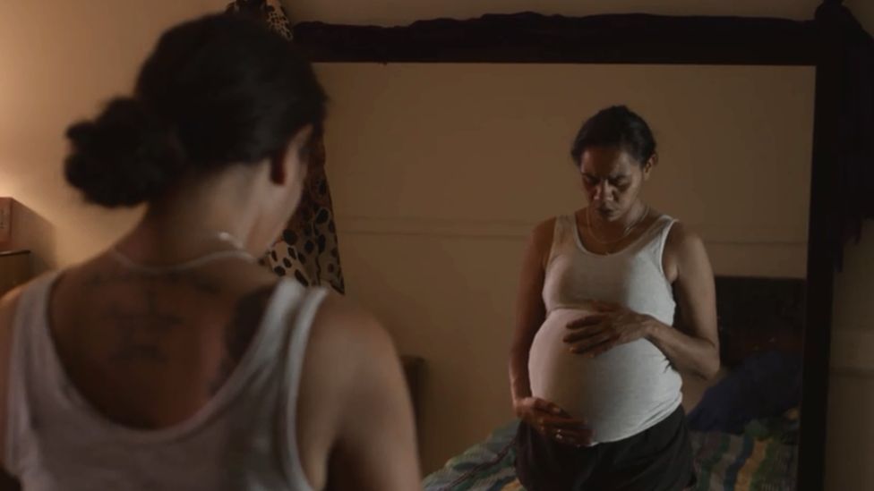 A pregnant indigenous Australian woman looks into a mirror while holding her stomach, in a still from a TV ad campaign