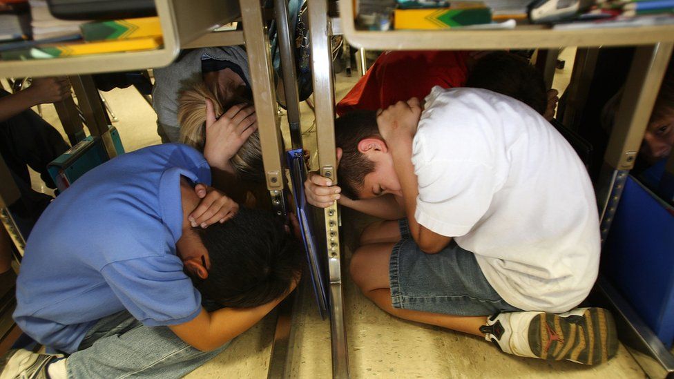 Two children crouch under their desks