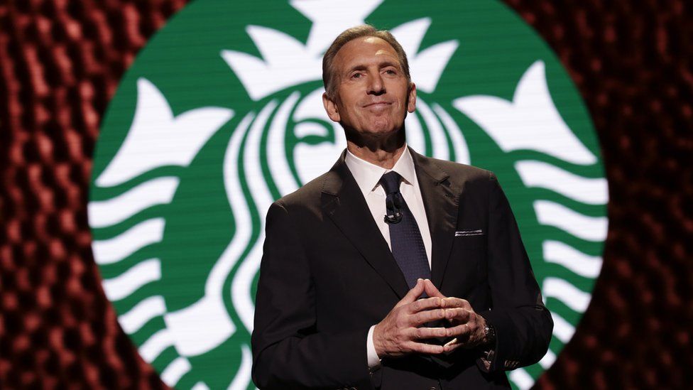 Schultz in front of Starbucks logo onstage in 2017